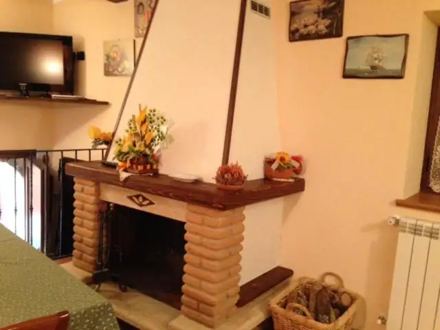 Soggiorno de Il Borgo 30 con camino rivestito in mattoni, mensola in legno, cesto di legna e televisore a parete.