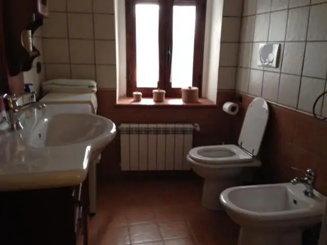 Bagno de Il Borgo 30 con doppio lavabo, finestra, radiatore e rivestimento in piastrelle chiare e terracotta.