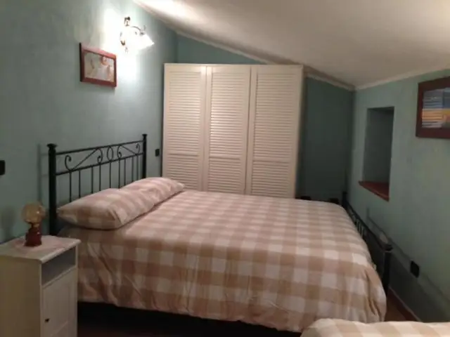 Camera matrimoniale de Il Borgo 30 con pareti verde chiaro, letto in ferro battuto con copriletto a quadri e armadio bianco a persiana.