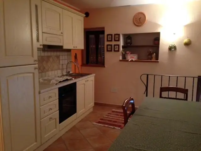 Cucina de Il Borgo 30 con mobili color crema, forno incassato, finestra e tavolo da pranzo in primo piano.
