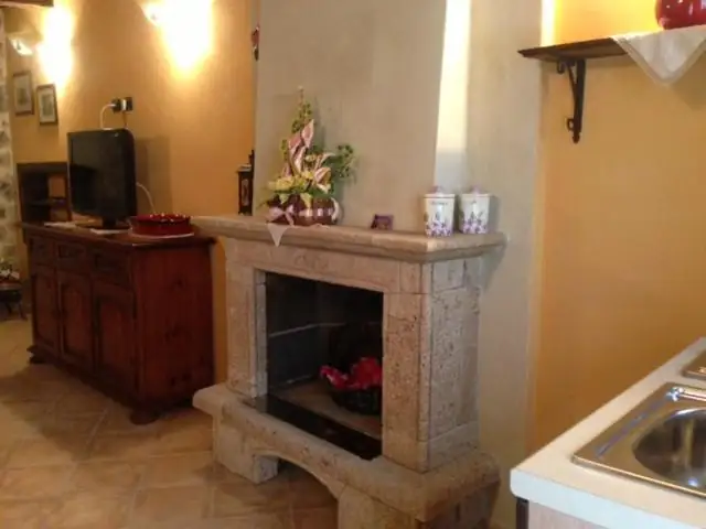 Camino in pietra chiara de Il Borgo 28 accanto all’angolo cottura, con credenza in legno e televisore.