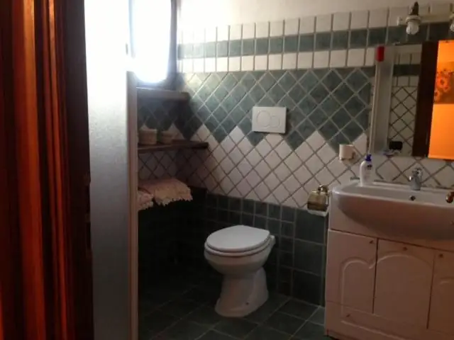 Bagno de Il Borgo 28 rivestito in piastrelle verdi e bianche, con lavabo, sanitari e mensola in legno.
