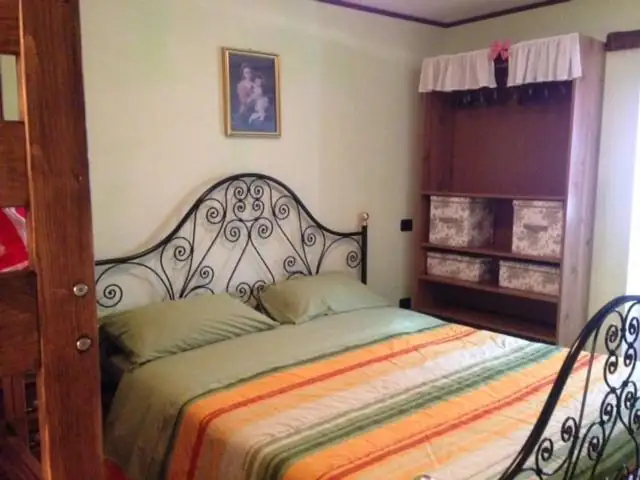 Camera matrimoniale de Il Borgo 28 con letto in ferro battuto nero, biancheria verde e arancio e armadio aperto a giorno.