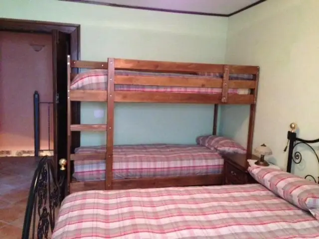 Letto a castello in legno accanto a un letto matrimoniale in ferro battuto, nella camera de Il Borgo 28 con pareti verde chiaro.