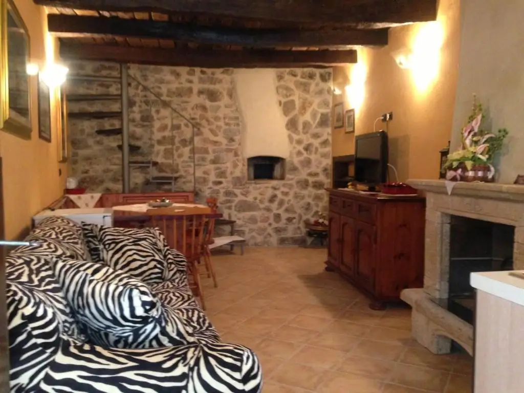 Zona giorno de Il Borgo 28 con travi di legno a soffitto, parete in pietra a vista, camino, credenza in legno e divano.