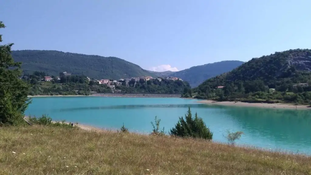 Veduta del lago di Castel San Vincenzo dall’alto: acqua turchese, colline boscose e il paese affacciato sul versante.