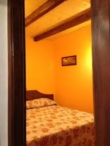 Camera da letto de Il Borgo 19 vista dalla porta: pareti gialle, travi di legno a vista e letto matrimoniale con copriletto a fiori.