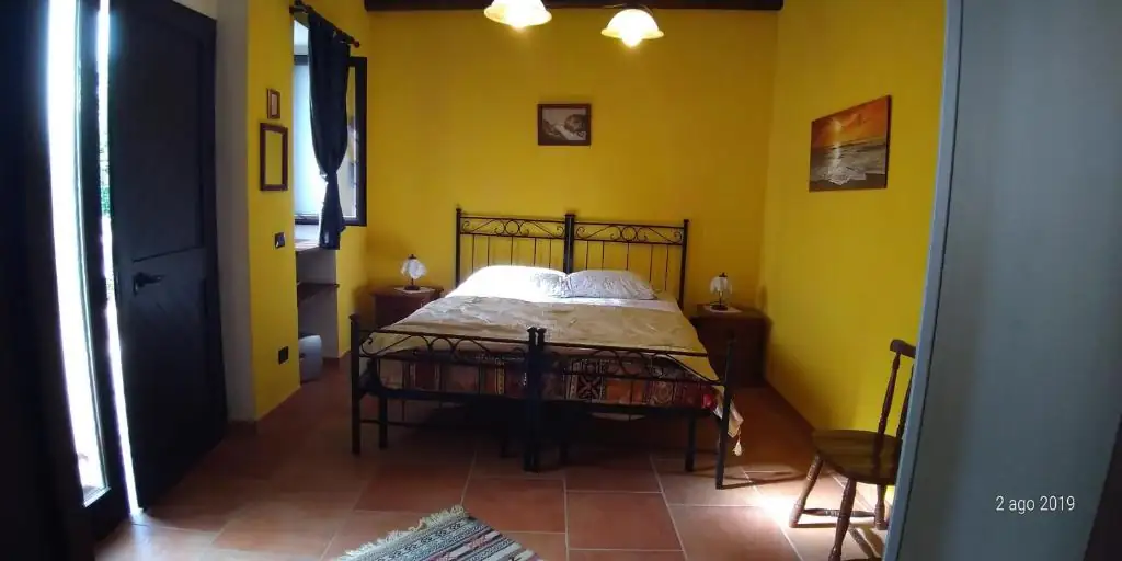 Camera de Il Borgo 31 con pareti gialle, letto matrimoniale in ferro battuto nero, due comodini e pavimento in cotto.