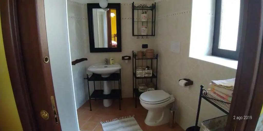 Seconda vista del bagno de Il Borgo 31, con finestra, asciugamani piegati e scaffale in ferro battuto.