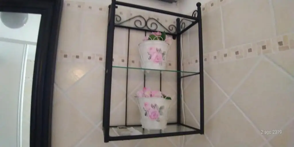Dettaglio del bagno de Il Borgo 31: mensola in ferro battuto con due vasetti di fiori sopra le piastrelle chiare.