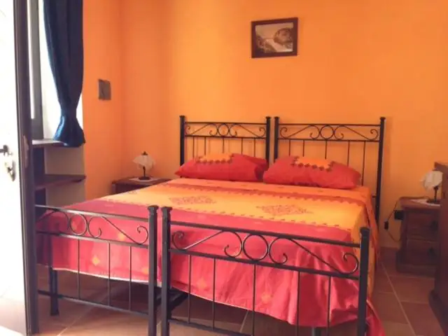 Seconda camera fotografata nella scheda de Il Borgo 31, con pareti arancio, letto matrimoniale in ferro battuto e biancheria rossa e gialla.