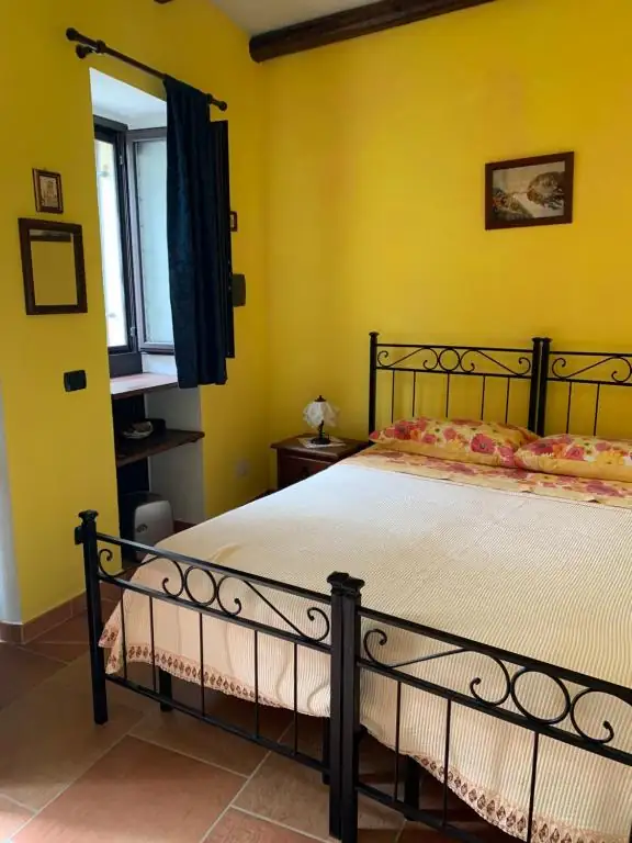 La stessa camera de Il Borgo 31 vista dal lato opposto: finestra con tenda blu, specchi alle pareti e letto matrimoniale in ferro battuto.