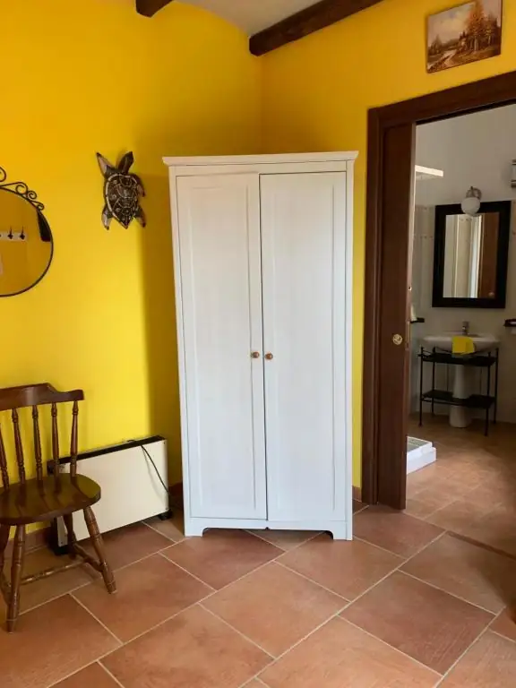 Armadio bianco a due ante nella camera de Il Borgo 31, con parete gialla e porta aperta sul bagno.