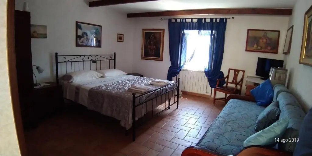 Camera ampia de Il Borgo 38 con letto matrimoniale in ferro battuto, finestra con tende blu, quadri alle pareti e divano azzurro sulla destra.