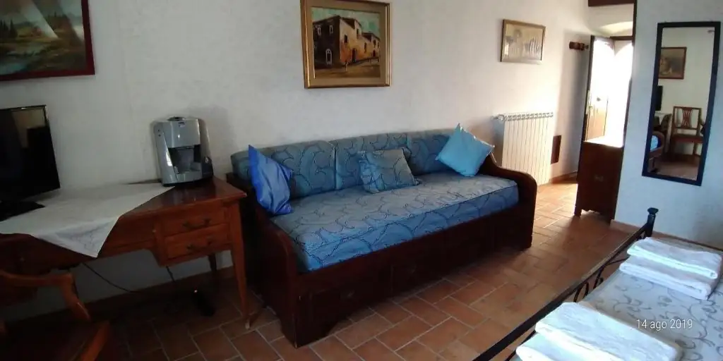 Angolo salotto de Il Borgo 38 con divano azzurro e cuscini, scrittoio in legno, macchina del caffè e televisore.