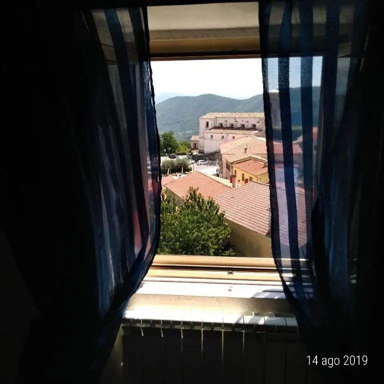 Veduta dalla finestra de Il Borgo 38: tetti in coppi del centro storico di Scapoli, un edificio storico e le montagne all’orizzonte.