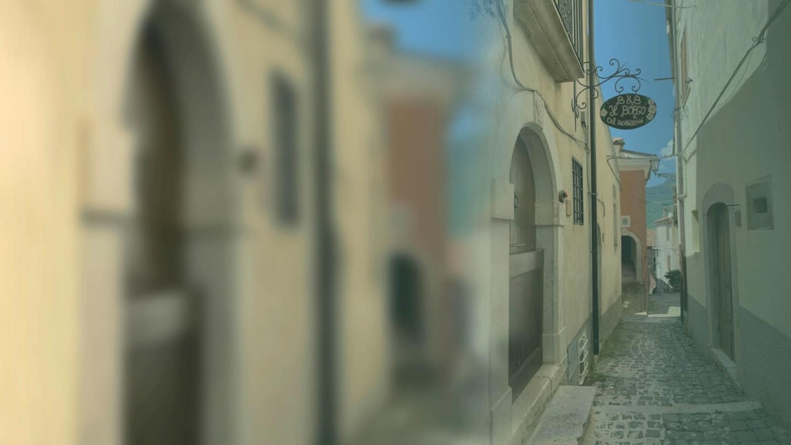 Un vicolo lastricato del centro storico di Scapoli fra case di pietra, con l’insegna in ferro battuto del B&B Il Borgo appesa a una facciata.